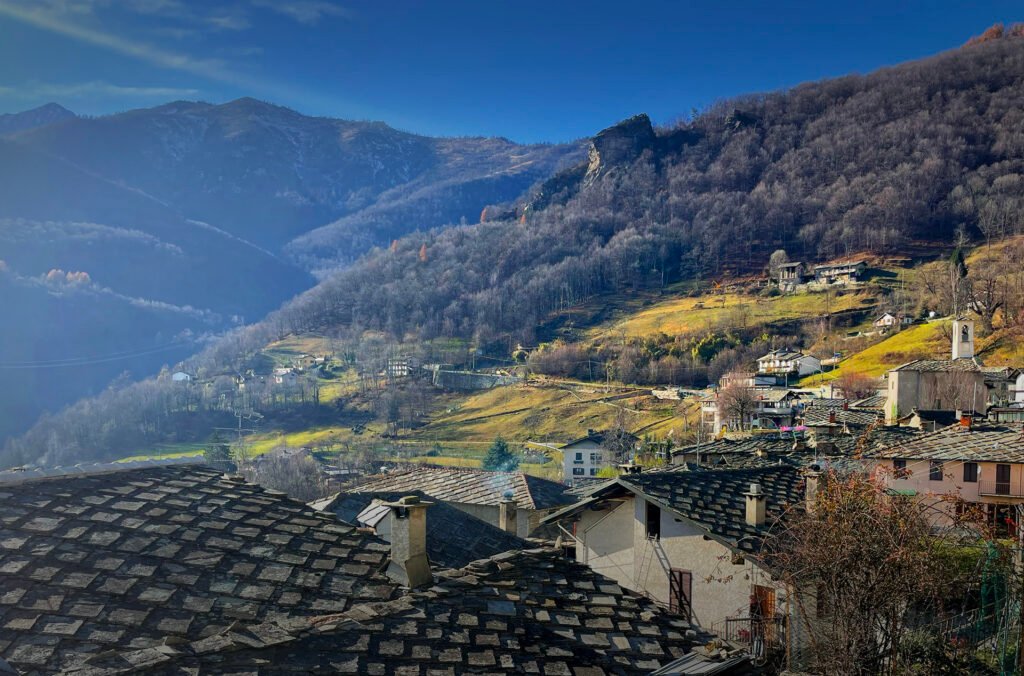 Stone rooftops of Rorà below a wooded mountainside