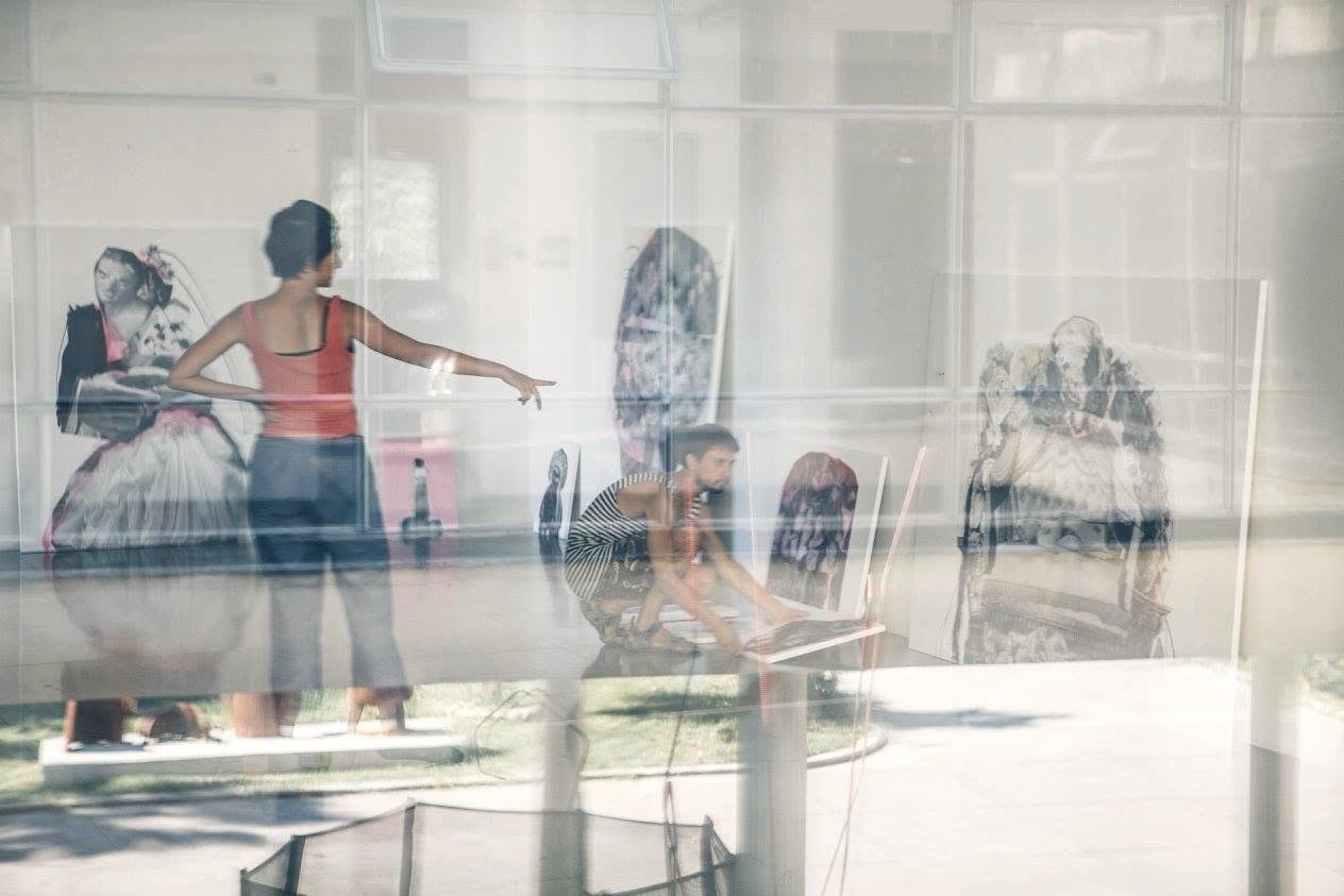 People arranging paintings in an exhibition space seen through reflective glass