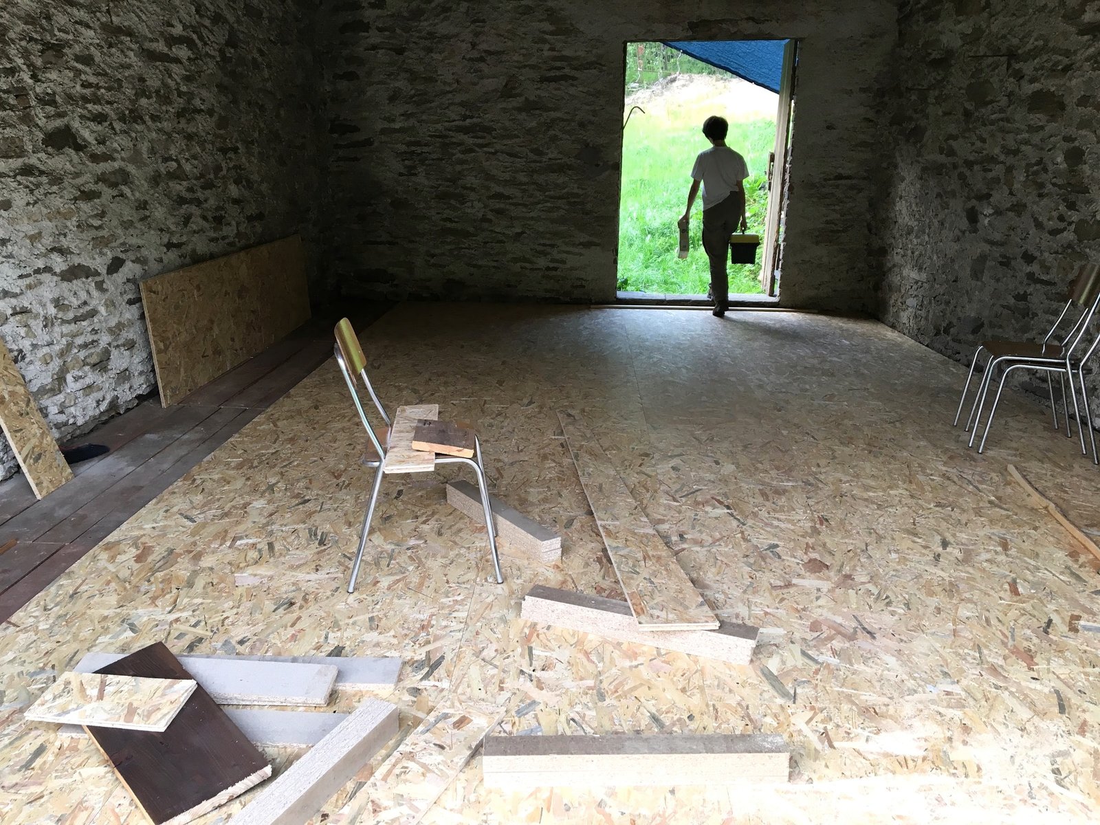 A person carrying tools through an unfinished stone room