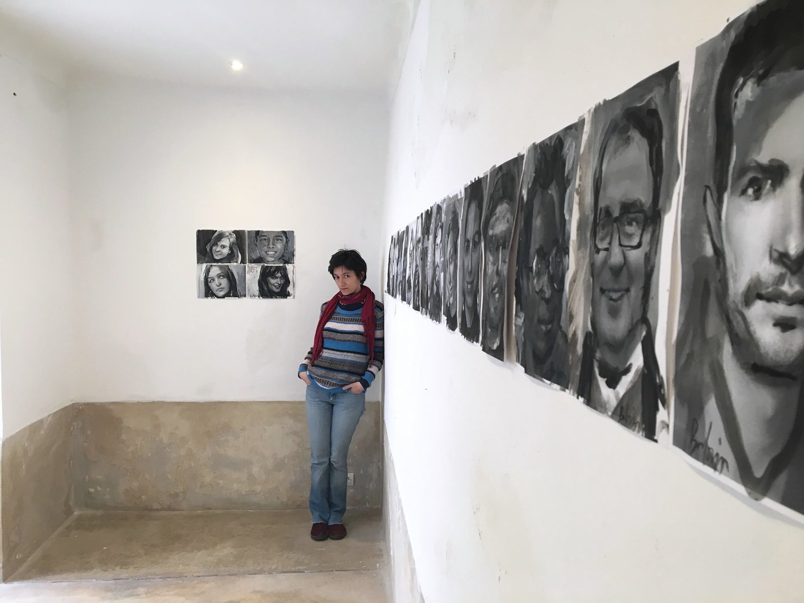 A woman standing beside a row of painted portraits in a gallery