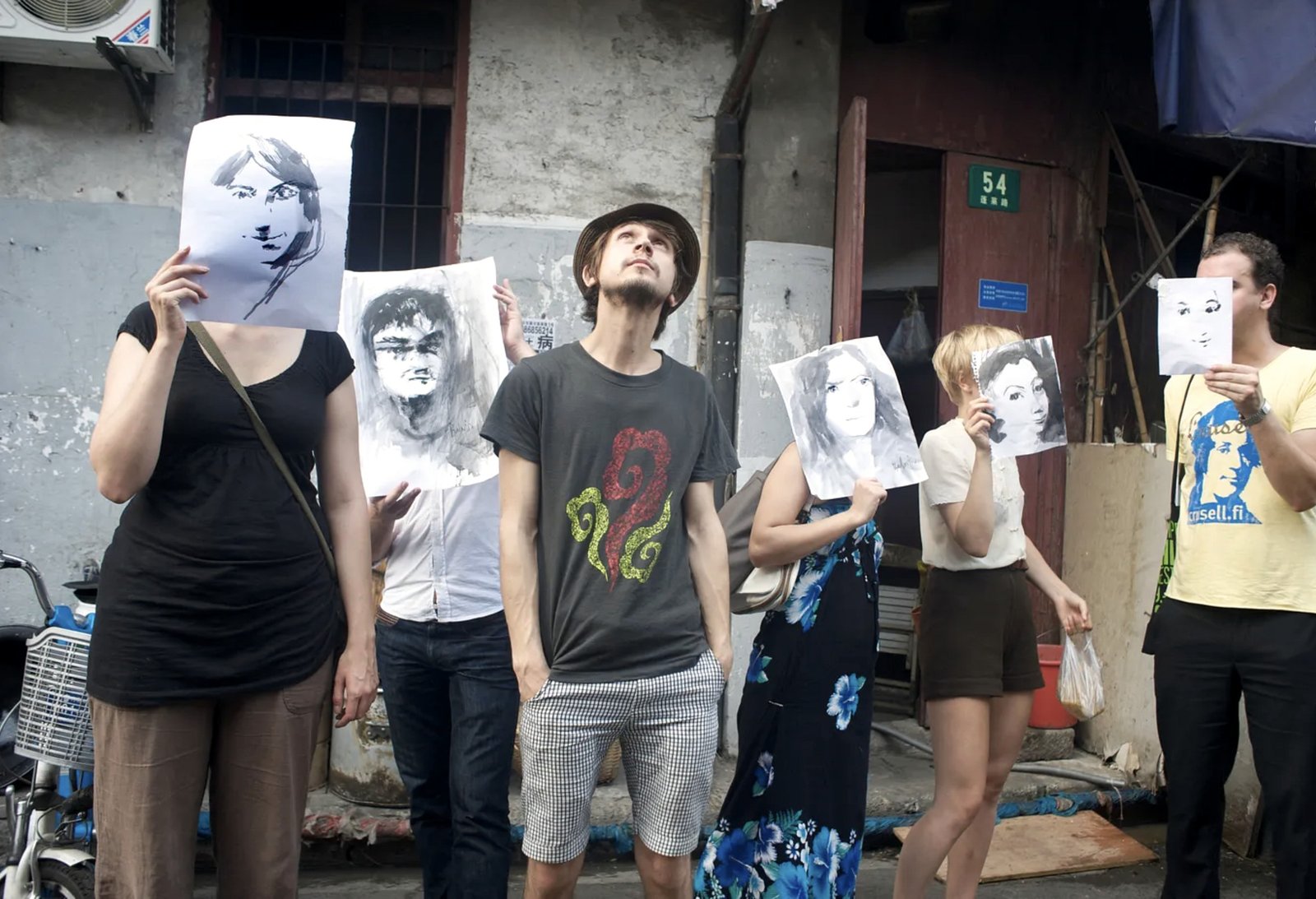 An artist and participants holding painted portraits in a street