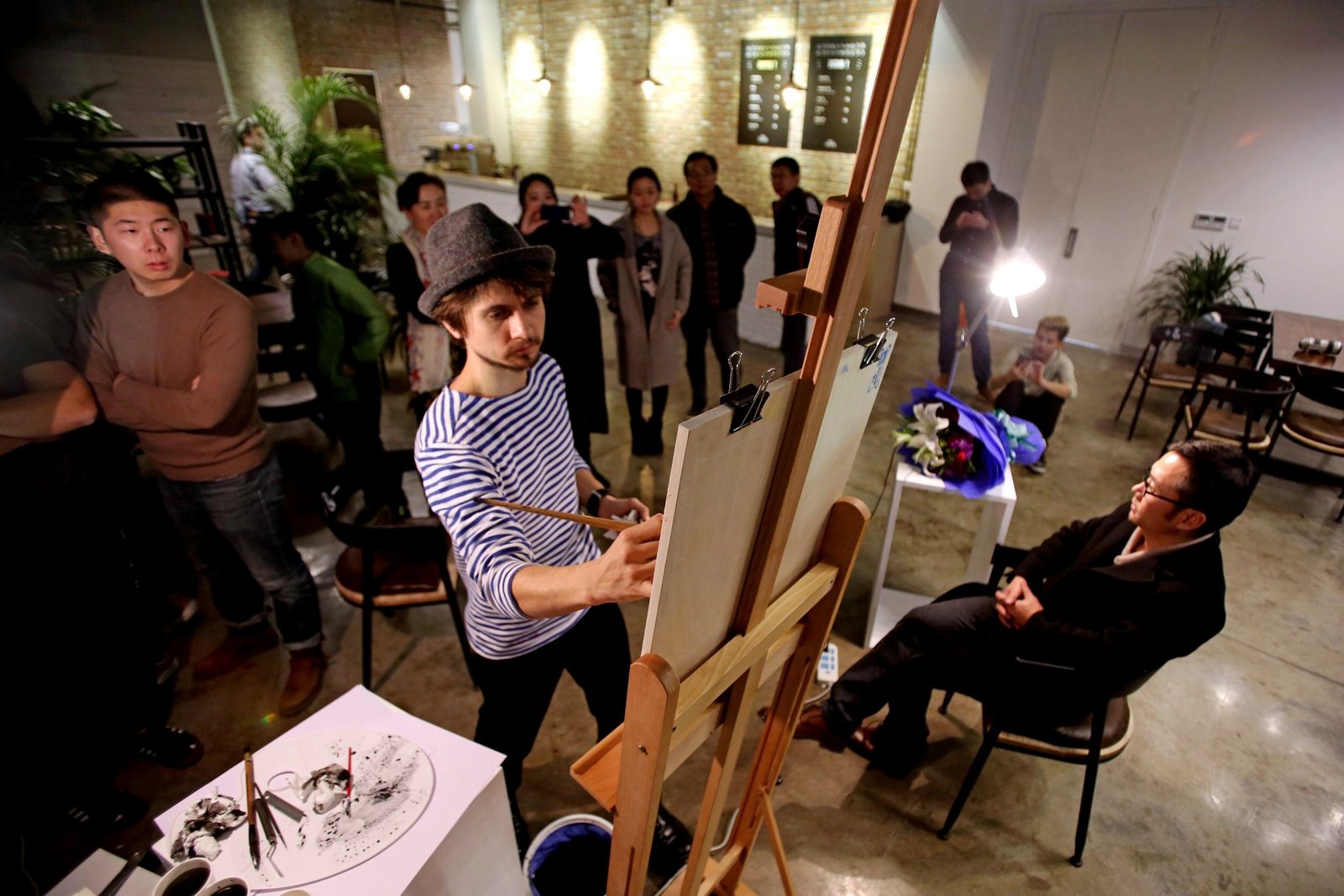 An artist drawing a seated participant at an easel while visitors watch