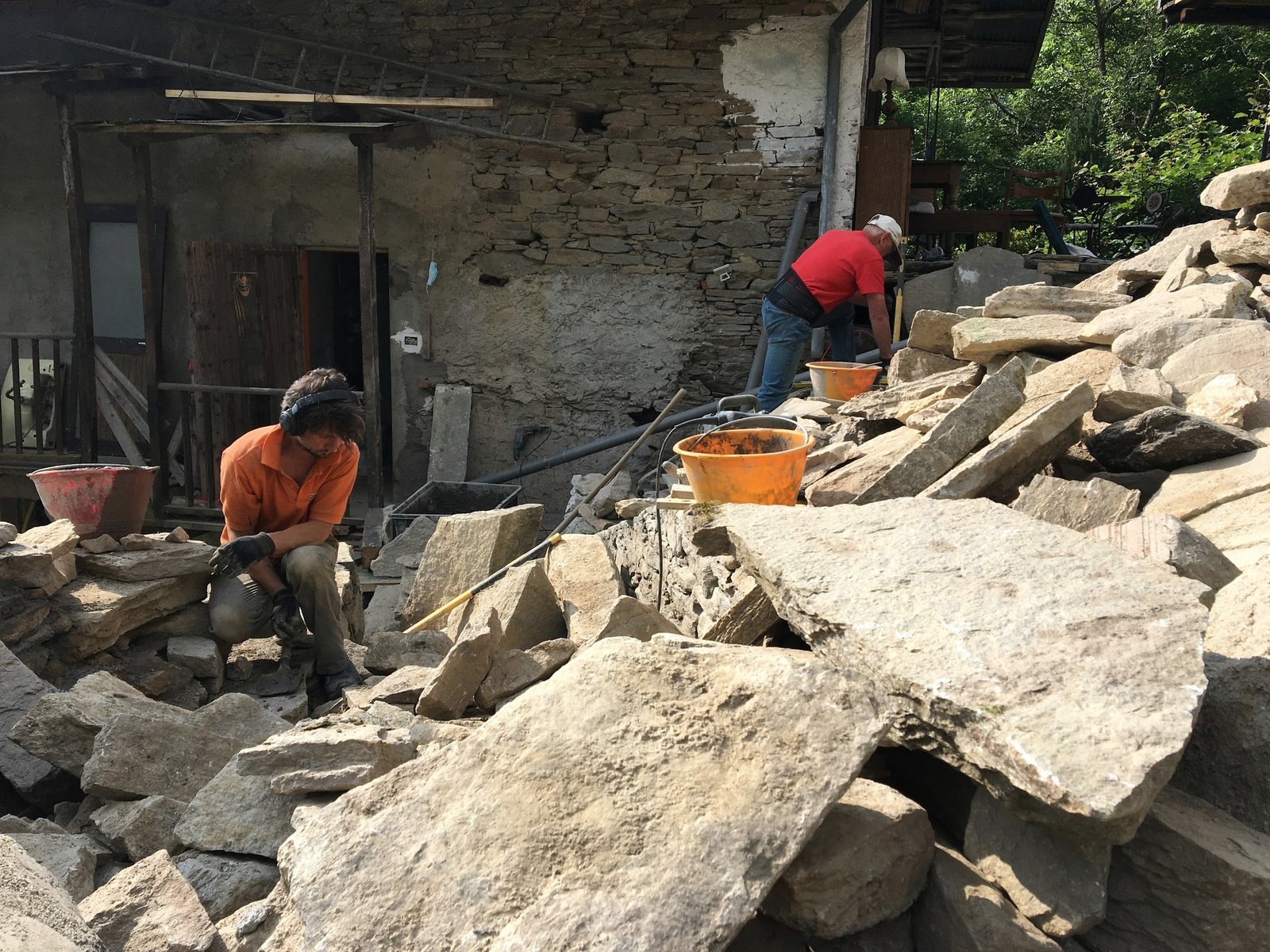 Two people restoring stonework beside the house