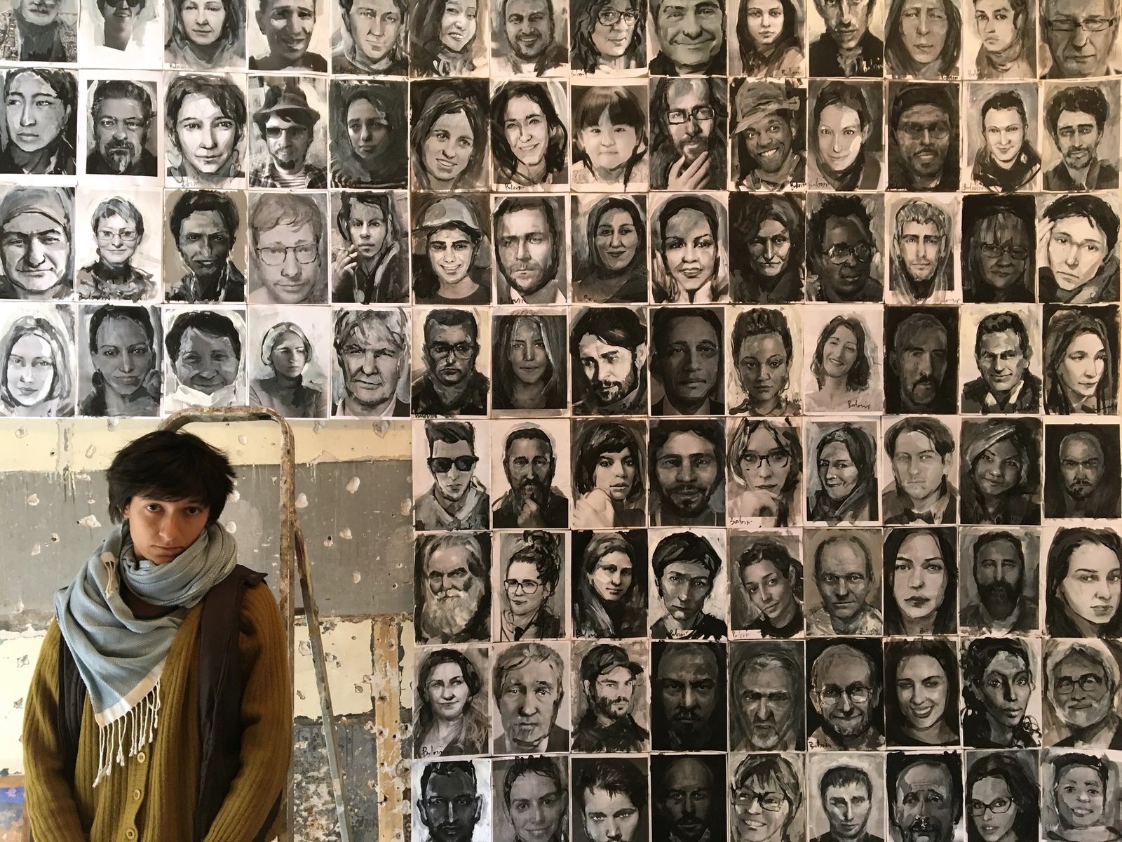 A woman beside a wall filled with painted portraits